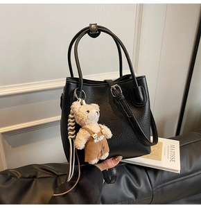 Detail of black lychee grain bucket bag featuring a cute teddy bear charm and leather strap