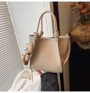 Detail of beige bucket bag with knotted handle, litchi leather, and cute bear charm