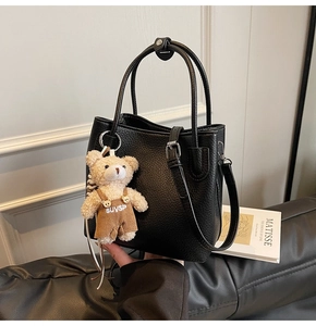 Detail of black lychee grain tote with silver hardware and a plush bear charm on a sofa