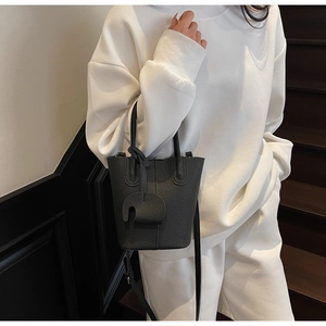 Borsa a secchiello grigio scuro con grana litchi indossata da una modella in abito bianco