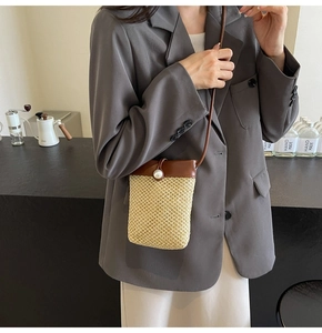 Detail of woven straw phone bag with leather flap and pearl closure on a grey blazer
