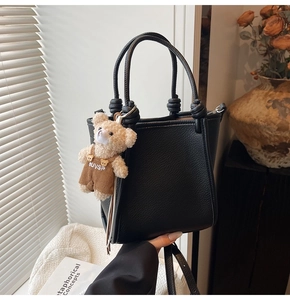 Detail of black lychee grain leather tote bag featuring knot handles and a cute bear charm
