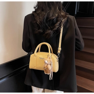 Detail of yellow lychee leather bowling bag with brown bear charm on model's shoulder