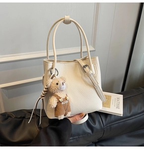 Close-up of off-white lychee grain leather bucket bag with cute bear charm and dual straps