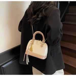 Detail of the high-gloss beige and pink shell bag featuring side gold pendant decor