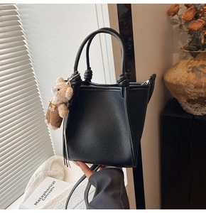 Detail of black litchi texture leather handbag with cute teddy bear charm pendant