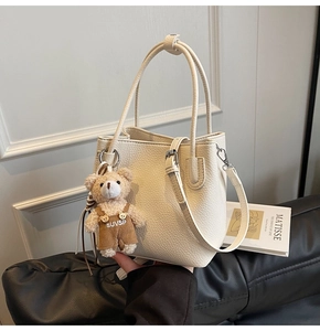 Detail of creamy white bucket bag on leather sofa with cute bear pendant accessory