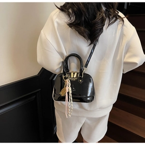 Close-up of black patent leather shell bag with gold hardware and woven charm