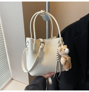 Detail of off-white lychee leather bucket bag with cute plush bear charm and silver hardware