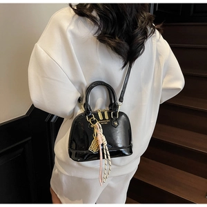 Close-up of black patent leather shell bag with gold hardware and woven charm