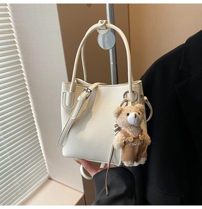 White lychee leather bucket bag with cute teddy bear charm on a metal display stand