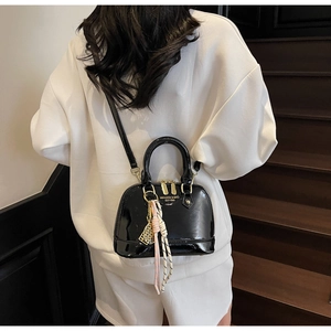 Detail of black patent leather shell bag with gold zippers and woven pendant on white hoodie