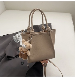 Flat lay of beige lychee leather bucket bag with cute bear charm and adjustable strap