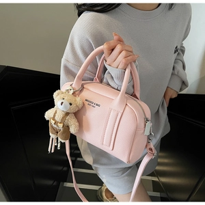 Pink lychee grain leather bowling bag with cute bear charm worn on stairs by model