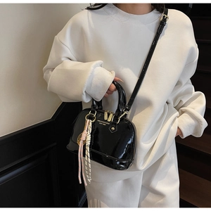 Close-up of black patent leather shell handbag with gold zippers and woven pendant