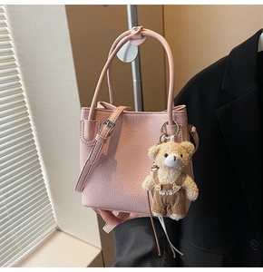 Detailed view of pink pebble grain handbag with cute plush bear charm on display