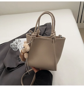 Detail of lychee pattern leather tote bag with a decorative knotted handle and bear charm