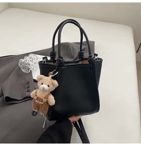 Detail of black pebble leather bucket bag featuring knot handles and a cute bear charm