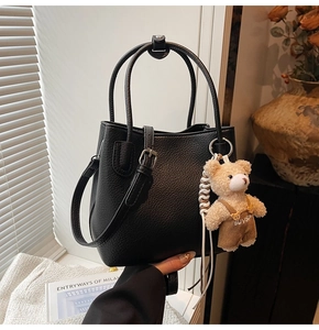 Detail of black lychee grain bucket bag with adjustable strap and plush bear charm