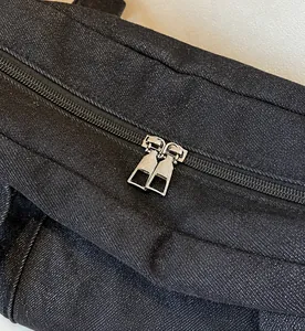 Dettaglio delle doppie cerniere in metallo argentato su borsa a spalla in denim nero