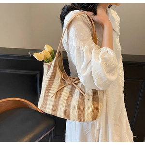 Detail of woven striped tote bag with bow accent and tulips held by model in lace dress