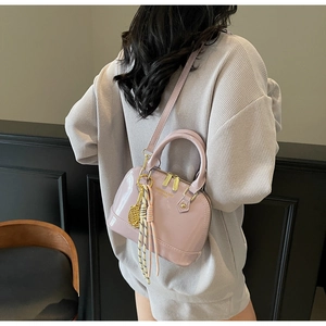 Detail of light pink patent leather shell bag with gold hardware and tassel charm