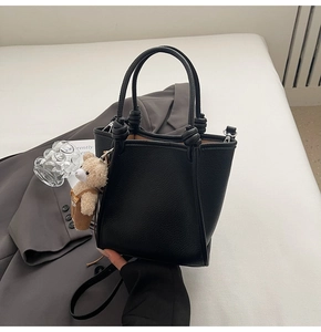 Detail of black pebbled leather bucket bag featuring knotted handles and bear charm