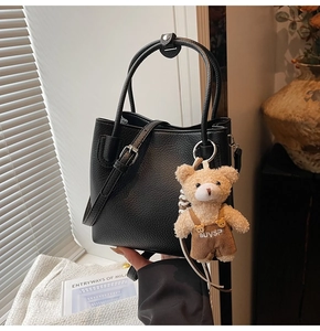Detail of black pebbled leather bucket bag with silver hardware and cute plush bear charm