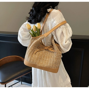 Detail of handwoven straw tote bag with brown leather straps and bow tie decoration