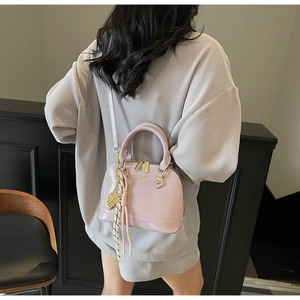 Light pink shell-shaped crossbody bag with gold lettering shown on a model