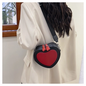 Close-up of a heart-shaped crossbody bag with a wide strap on a beige suit