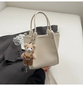 Close-up of cream white bucket bag with pebble texture leather and bear charm