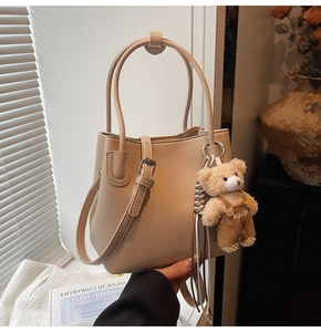Detail view of beige pebbled leather bucket bag with a cute teddy bear charm