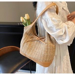 Detail of hand-woven straw tote bag featuring a cute bow and brown leather shoulder strap