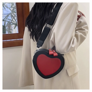 Detail of a heart-shaped PU leather crossbody bag in red and black on a beige blazer