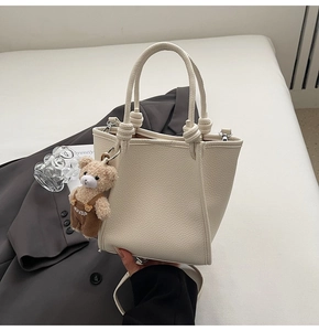 Detail view of cream-colored lychee texture leather handbag with bear charm and knot handle