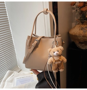 Detailed macro view of beige pebble grain leather bucket bag with cute plush bear charm
