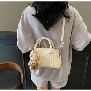 Cream pebbled crossbody bowling bag with cute teddy bear charm shown on a model
