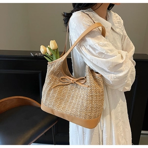 Detail of hand-woven straw tote bag with brown leather handles and a bow accent