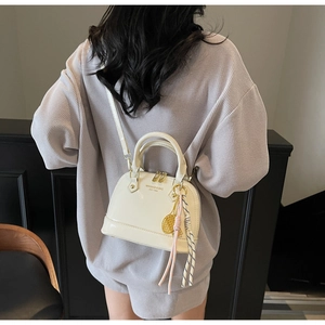 Rear view of a model wearing a glossy beige shell-shaped handbag with a gold-tone pendant