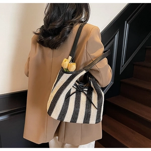 Detail of striped woven tote bag featuring a black bow tie and leather shoulder straps