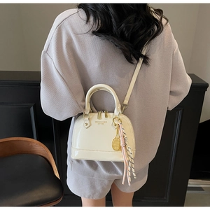 Detail of off-white shell handbag featuring a gold tennis racket charm and silk scarf