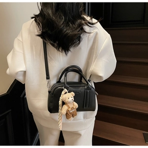 Detail of black lychee grain leather boston bag with a cute teddy bear charm on strap