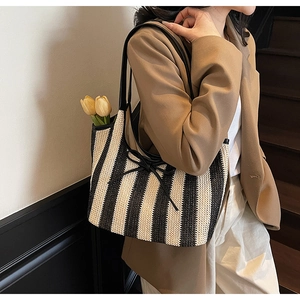 Detail of striped woven tote bag with black leather shoulder straps and bow knot detail