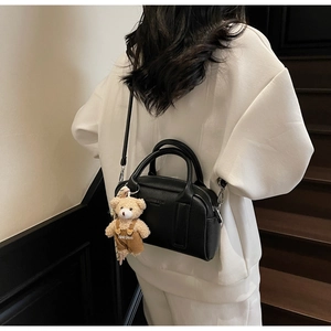 Model wearing black lychee leather bowling bag with cute bear charm on a wooden staircase