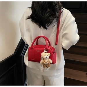 Close-up of red lychee leather Boston bag with teddy bear charm and logo print