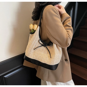 Detail of woven straw tote bag with black leather straps and a delicate bow accent