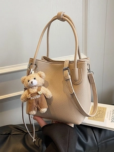 Chic beige lychee leather bucket bag with plush bear charm and adjustable shoulder strap