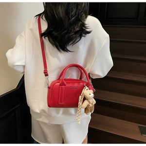 Red pebbled leather bowling bag with cute teddy bear charm shown on a casual model