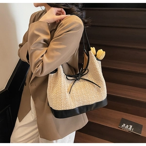 Detail of woven tote bag featuring black leather base and delicate bow decoration